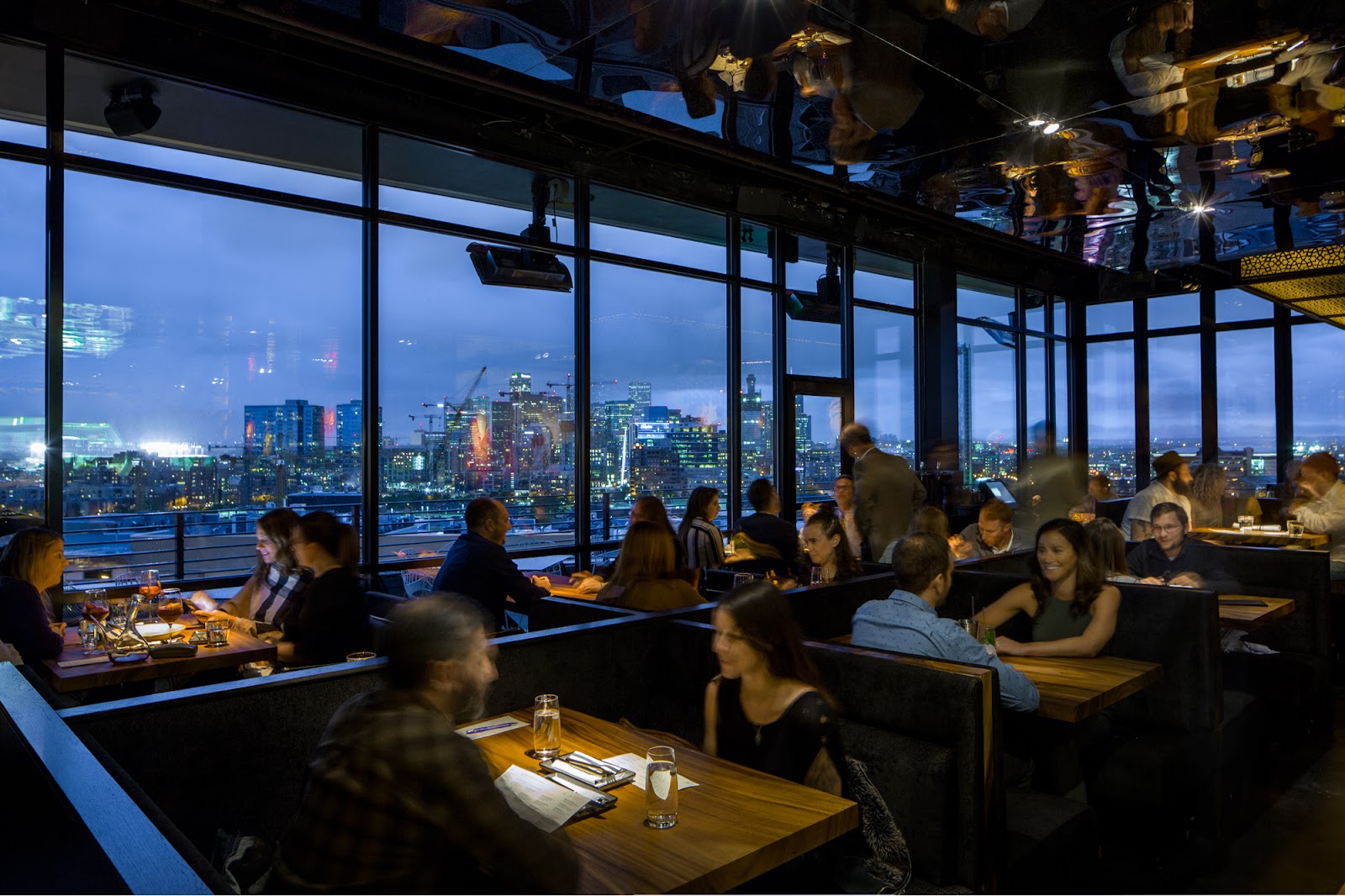 A Denver rooftop dining terrace at dusk with the skyline and the Rockies behind