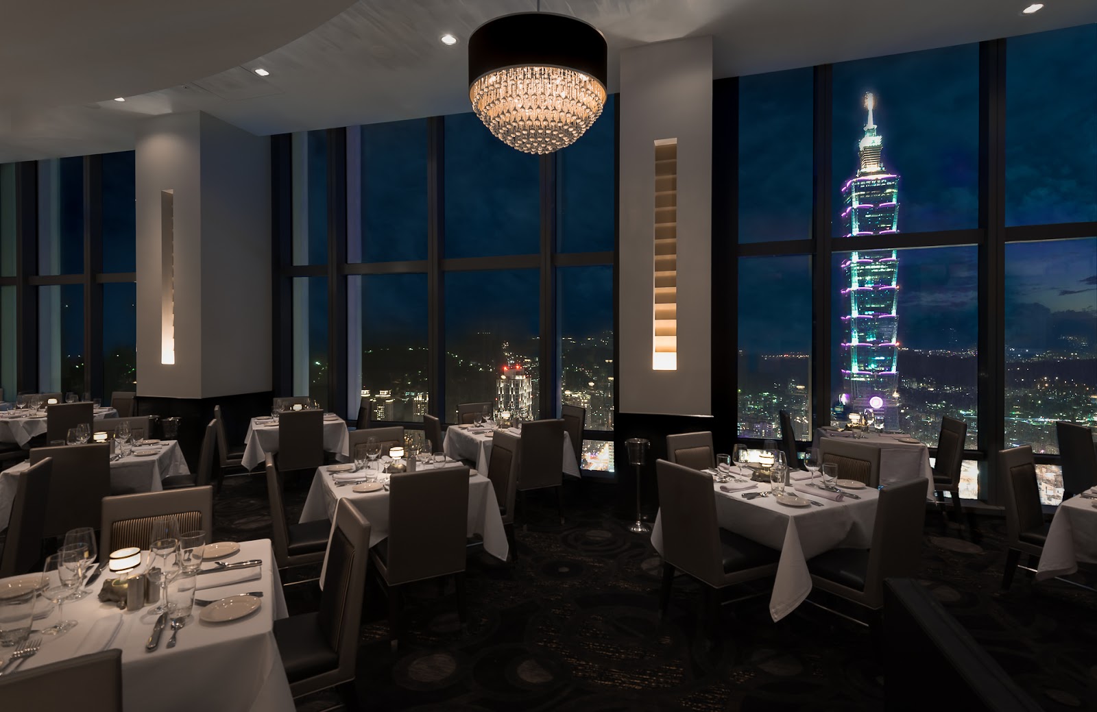 Taipei 101 lit at dusk seen from a high restaurant window in Xinyi