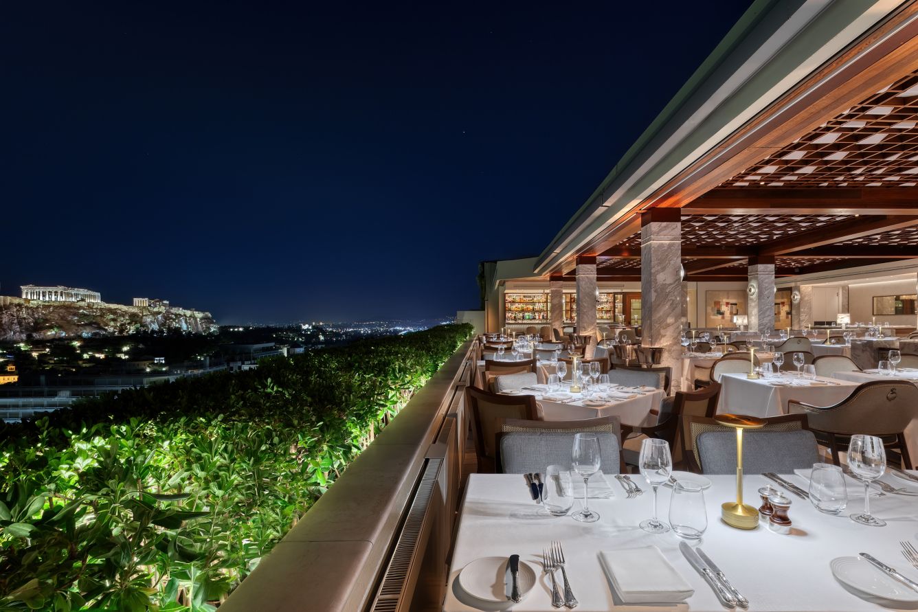 A private window table with the lit Acropolis beyond, set for a proposal in Athens