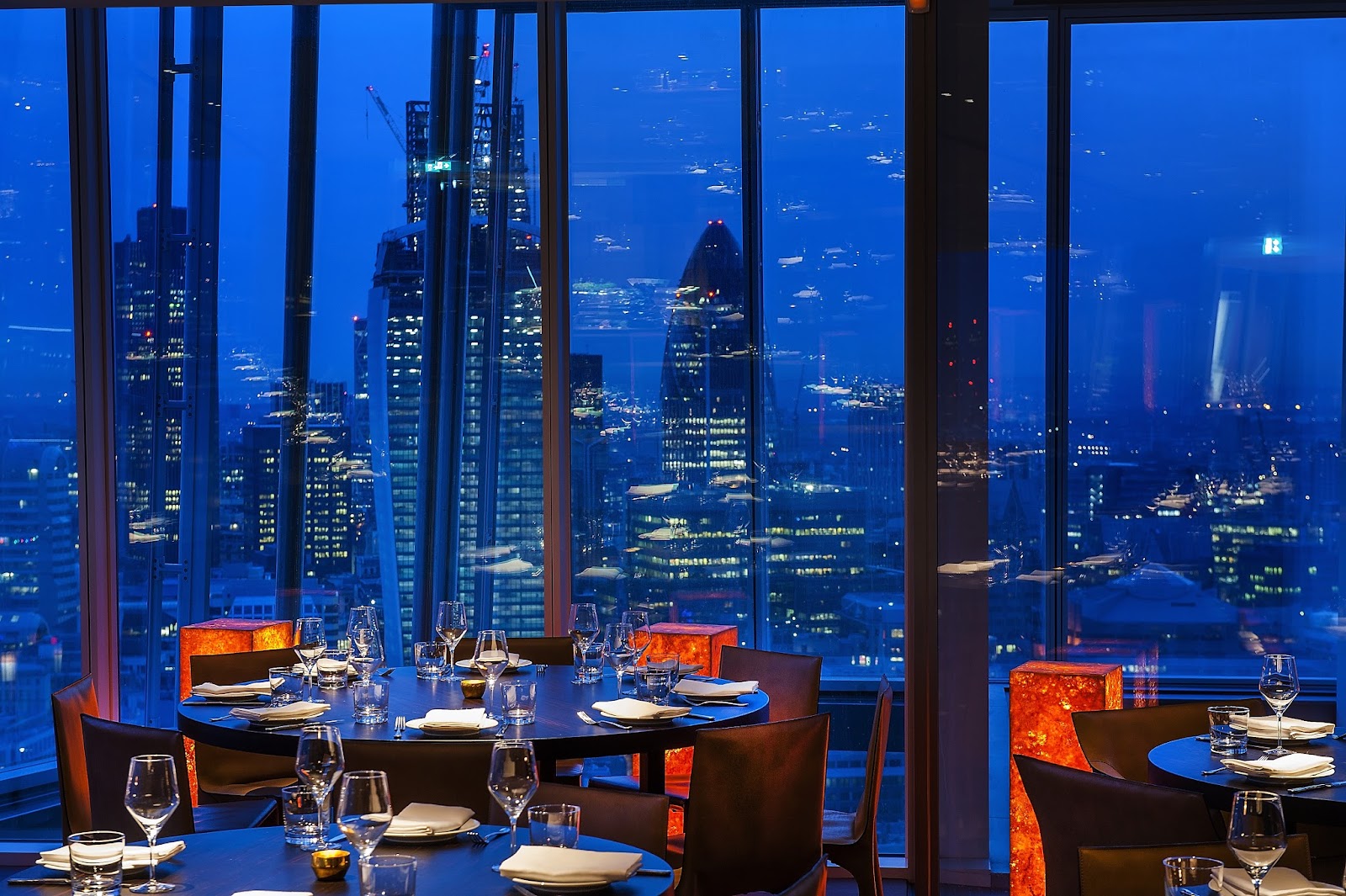 A top-floor dining room with the London skyline at dusk through floor-to-ceiling glass